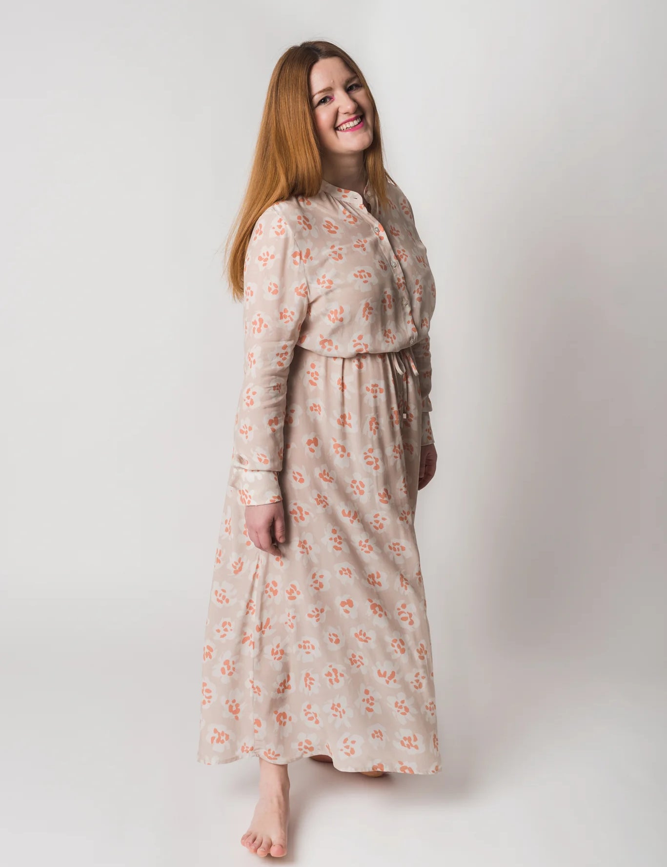 Frau lacht in geblümtem Kleid auf weißem Hintergrund.