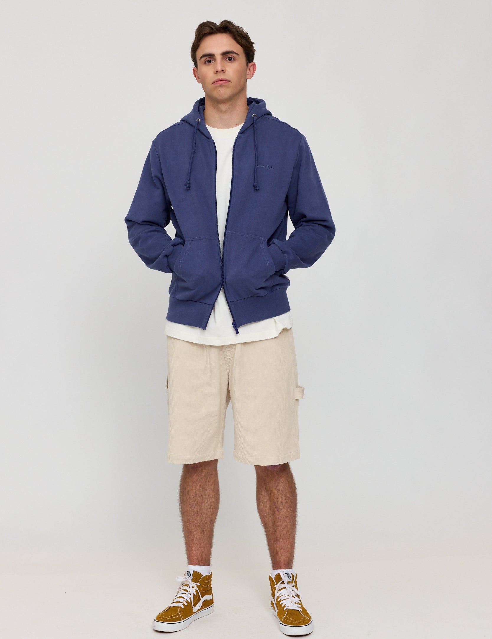 Mann in blauer Jacke und beigen Shorts steht