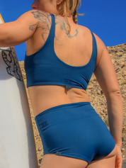 Frau in blauem Sportoutfit hält Surfbrett.