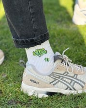 Bein in Jeans, weiße Socke mit Krokodil, Gras-Hintergrund.