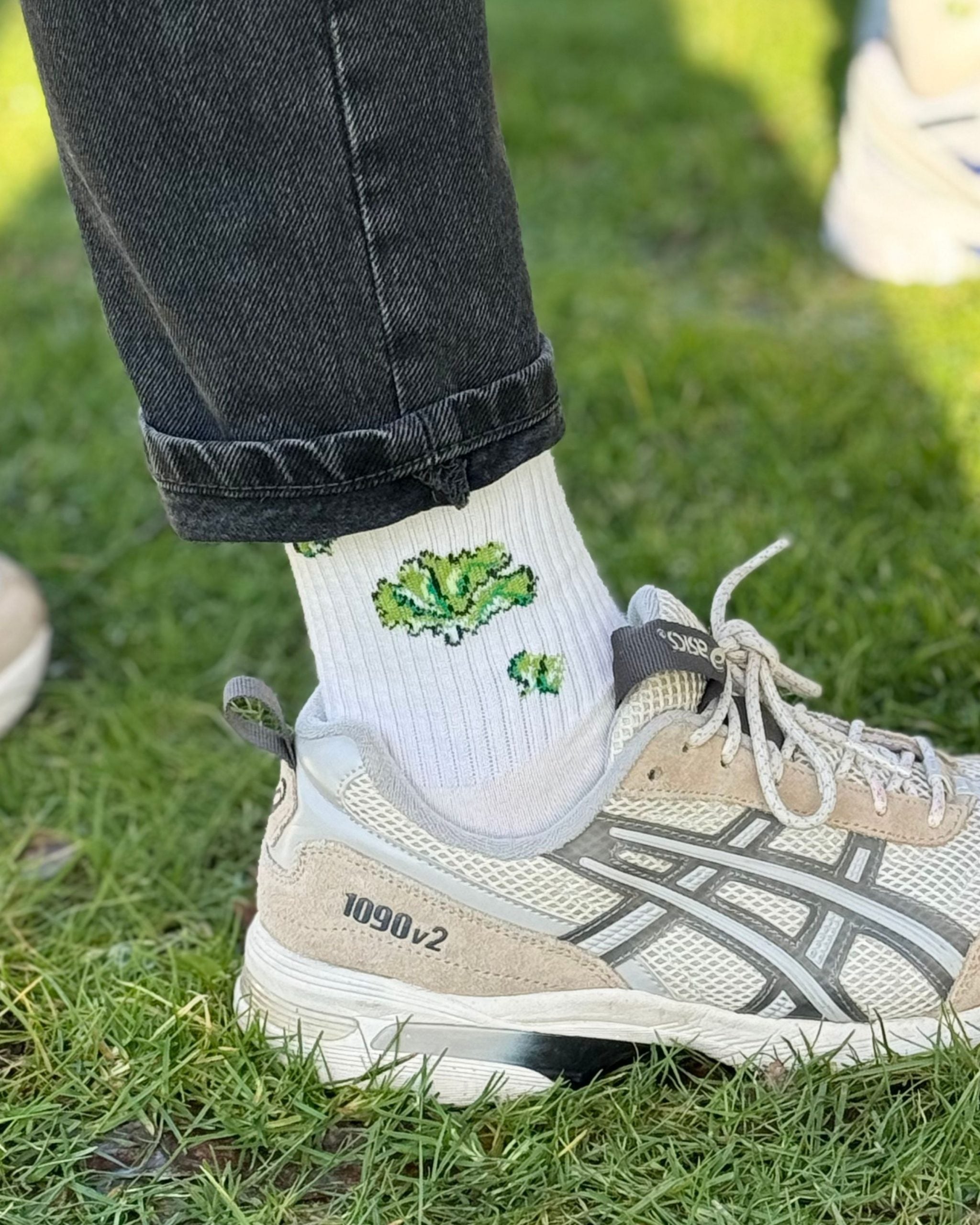 Bein in Jeans, weiße Socke mit Krokodil, Gras-Hintergrund.