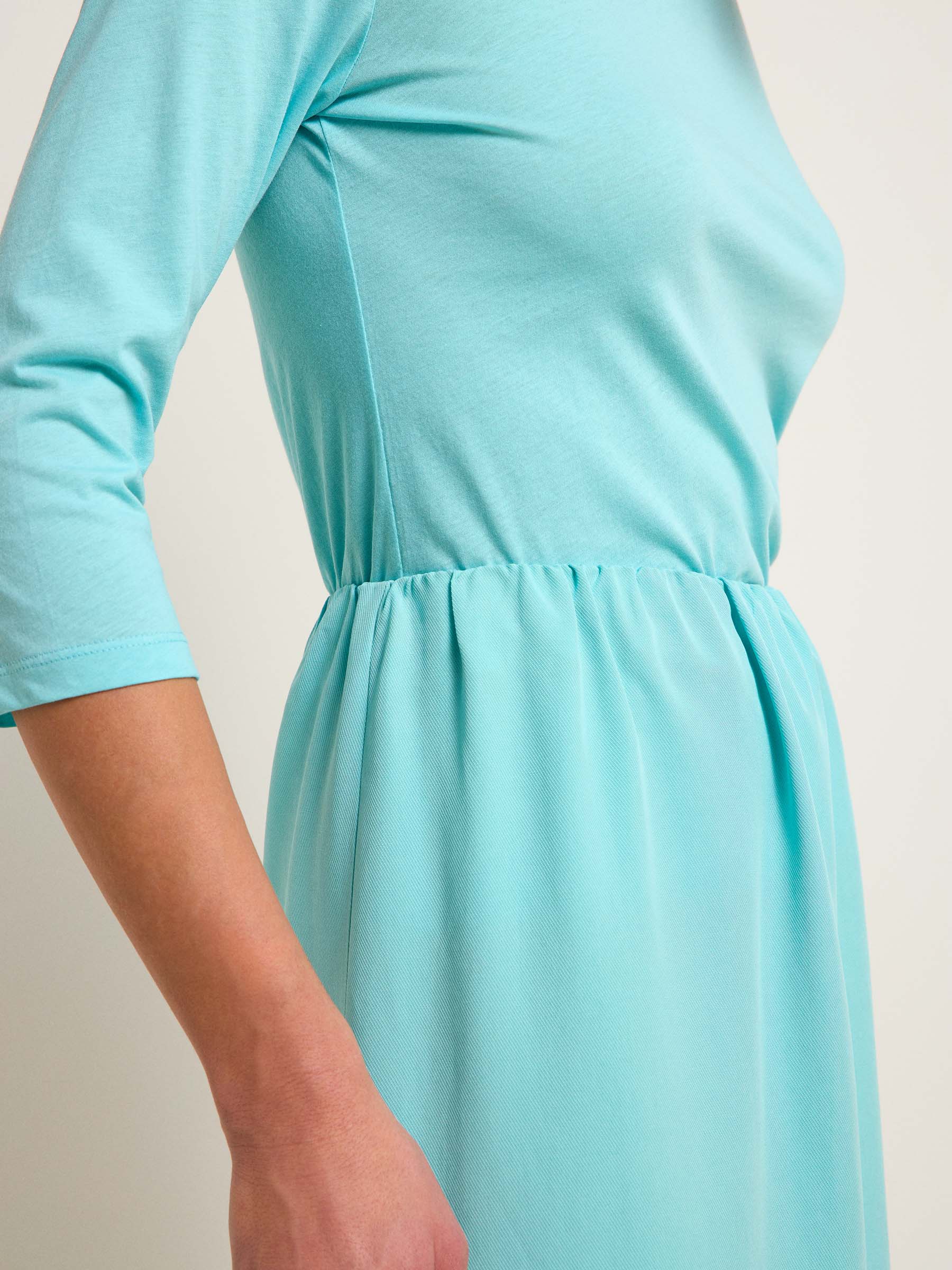 Person trägt türkises Kleid mit Taillendetail.