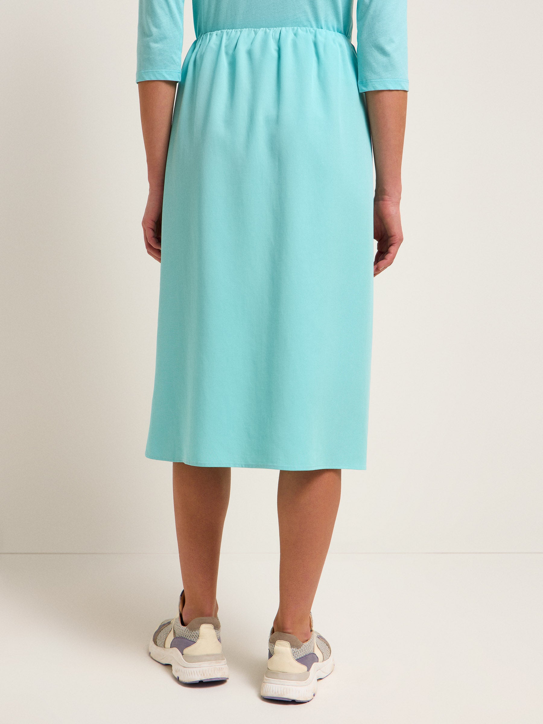Frau in türkisem Kleid und Sneakers von hinten.
