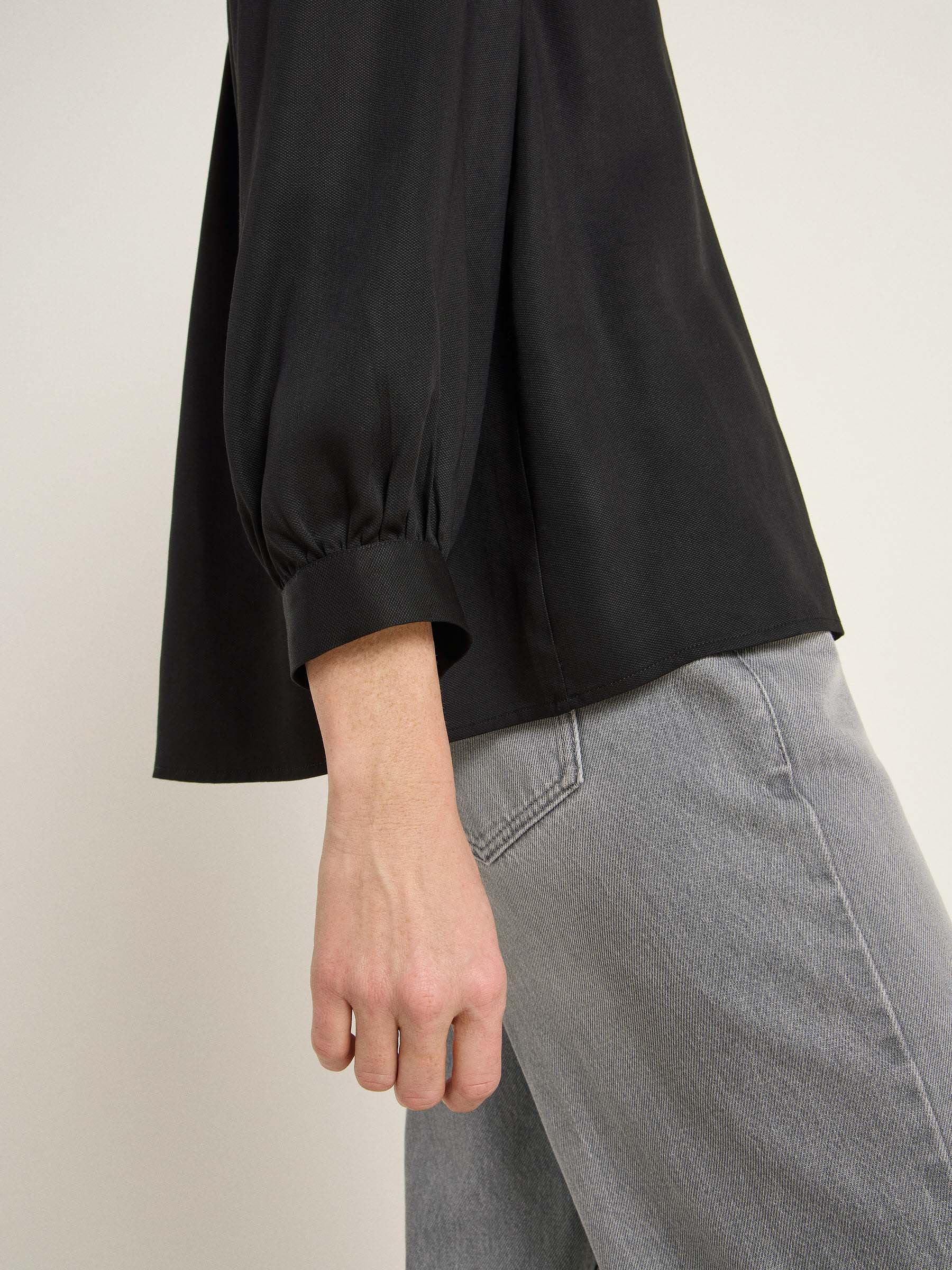 Detailaufnahme von Hand, schwarze Bluse, graue Hose
