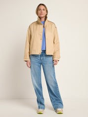 Frau in Jeans und beiger Jacke steht gerade