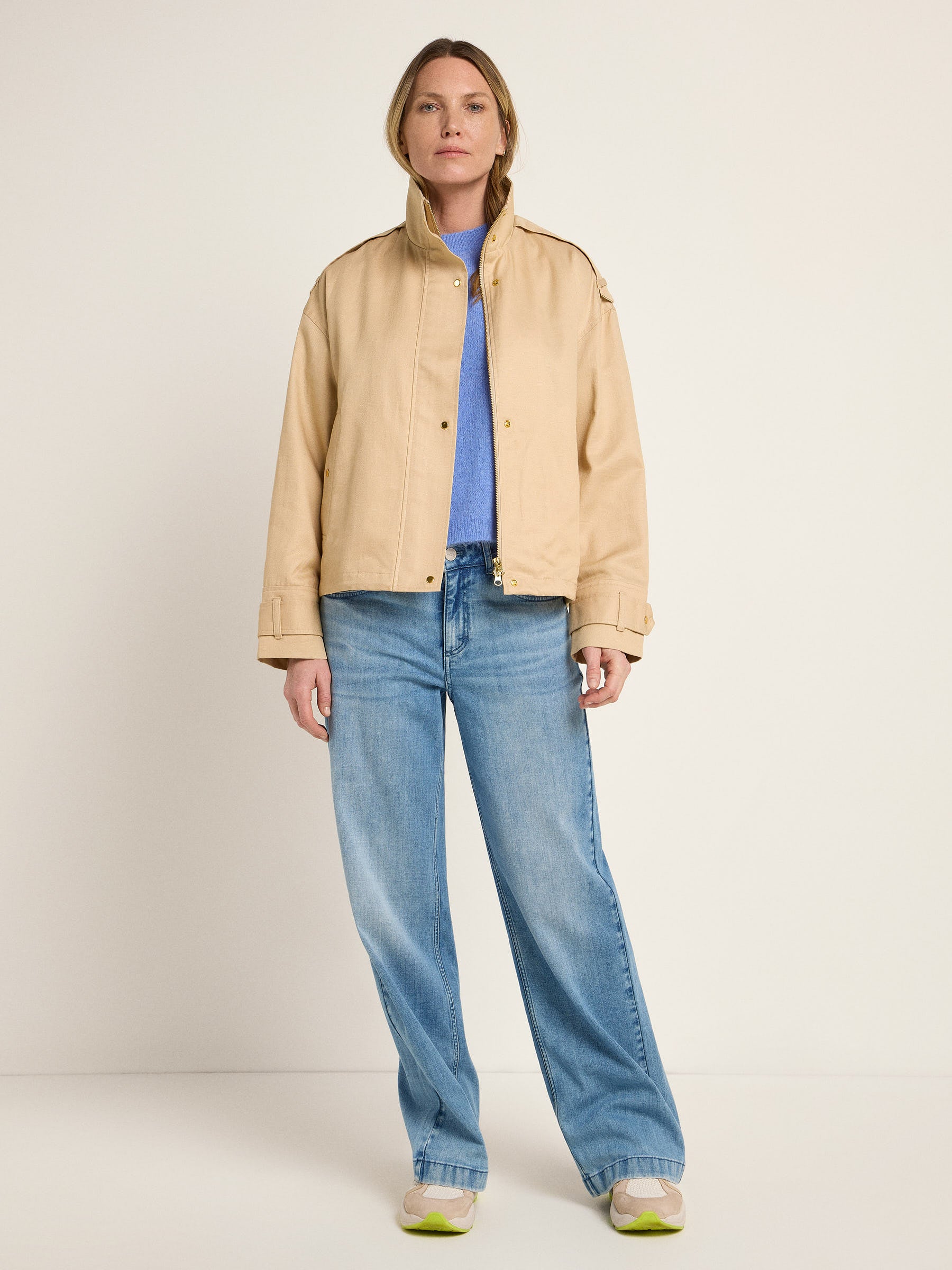 Frau in Jeans und beiger Jacke steht gerade