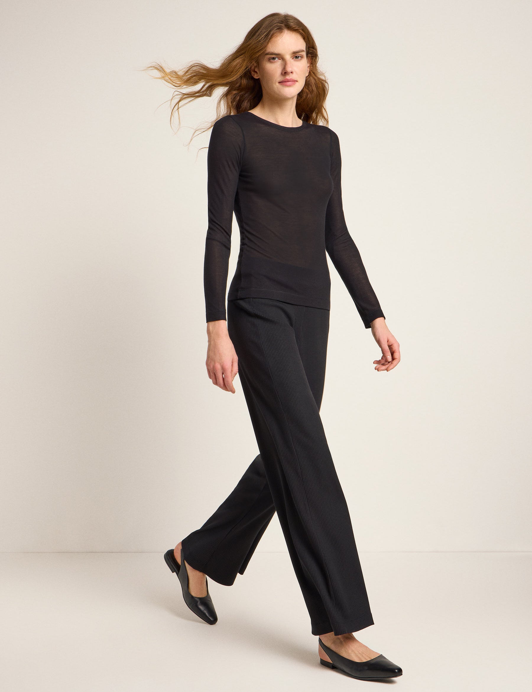 Frau im schwarzen Outfit läuft vor neutralem Hintergrund