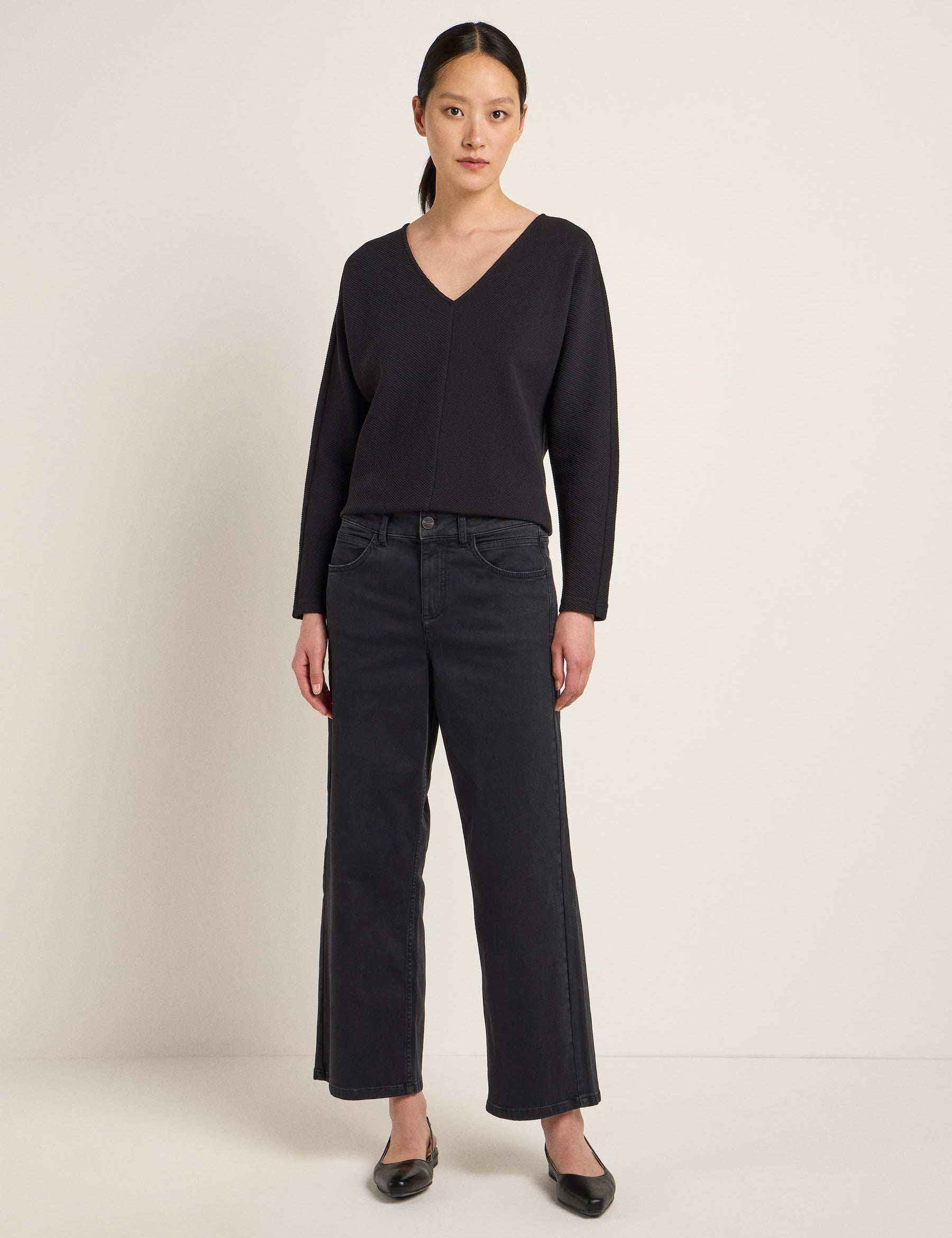 Frau in schwarzer Hose und Pullover steht