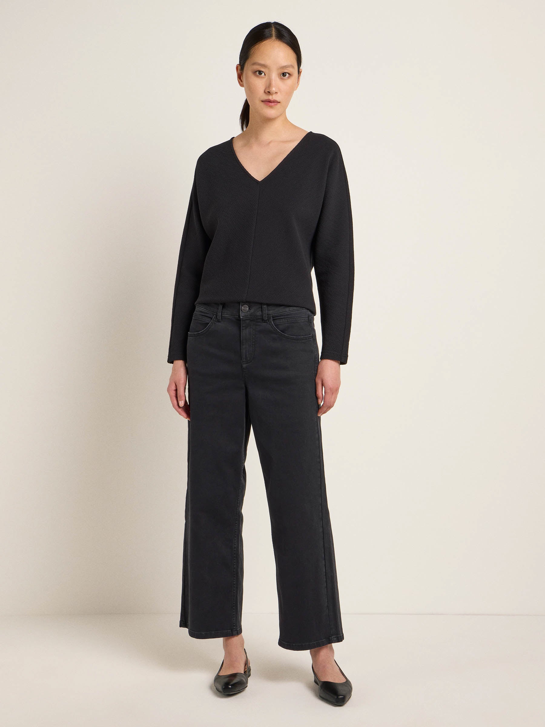 Frau in schwarzer Hose und Pullover steht