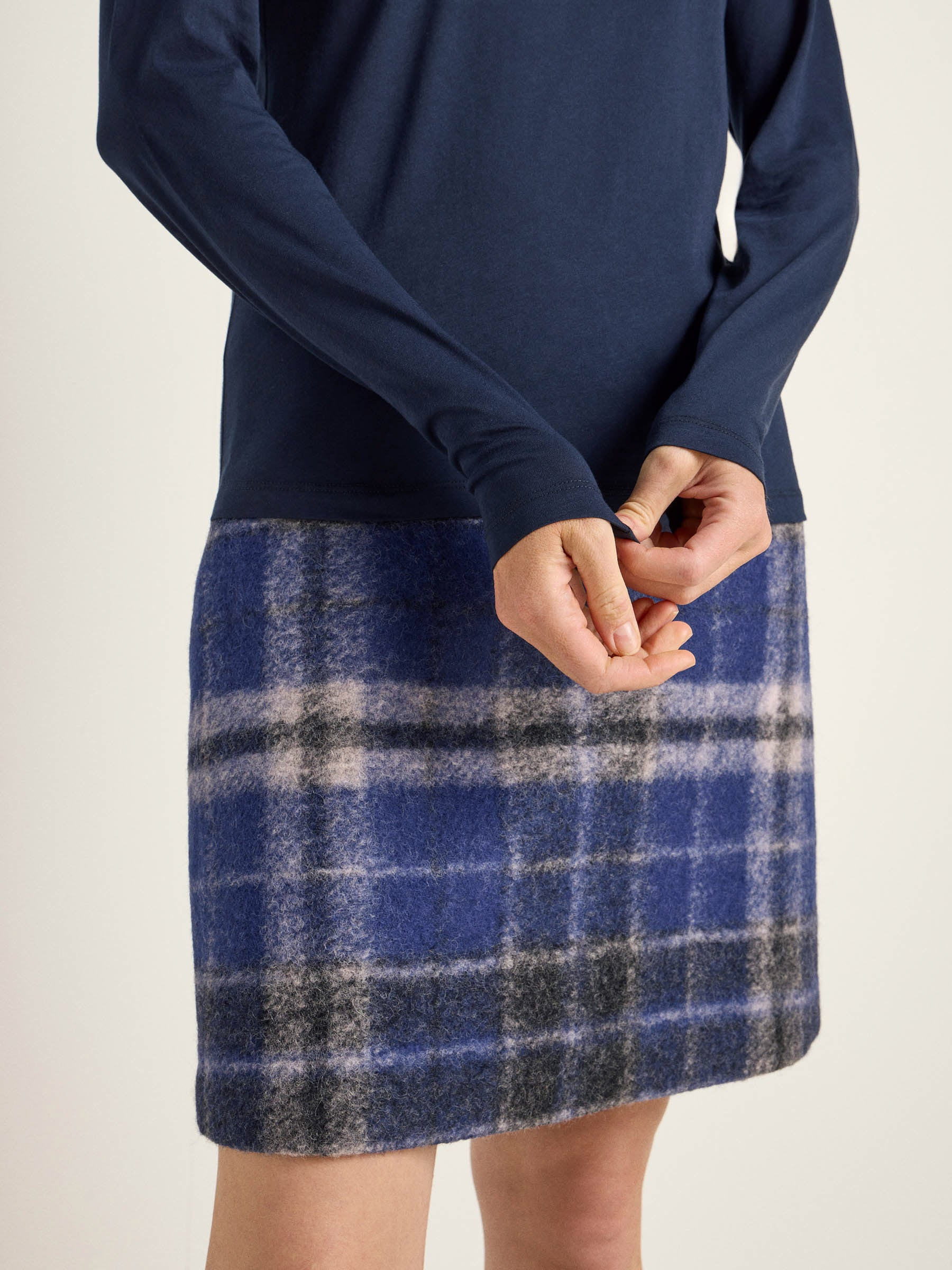 Person trägt blaues Oberteil und karierten Rock