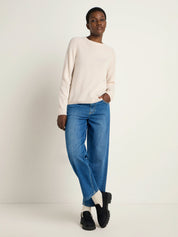 Frau in beigem Pullover und blauen Jeans steht