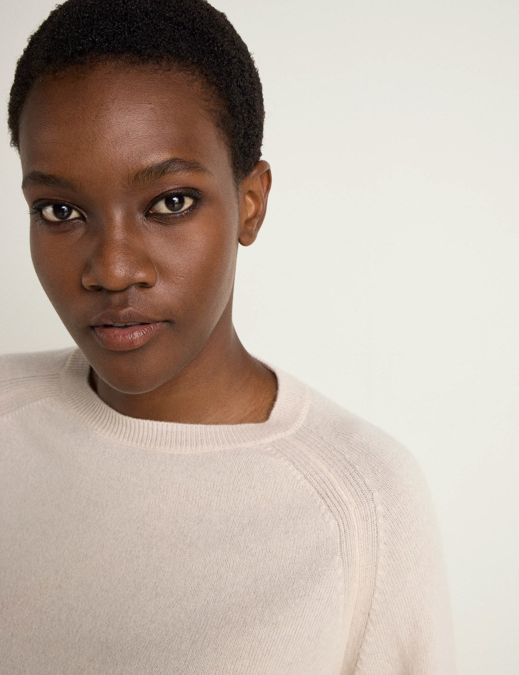 Junge Frau in beigem Pullover blickt in Kamera