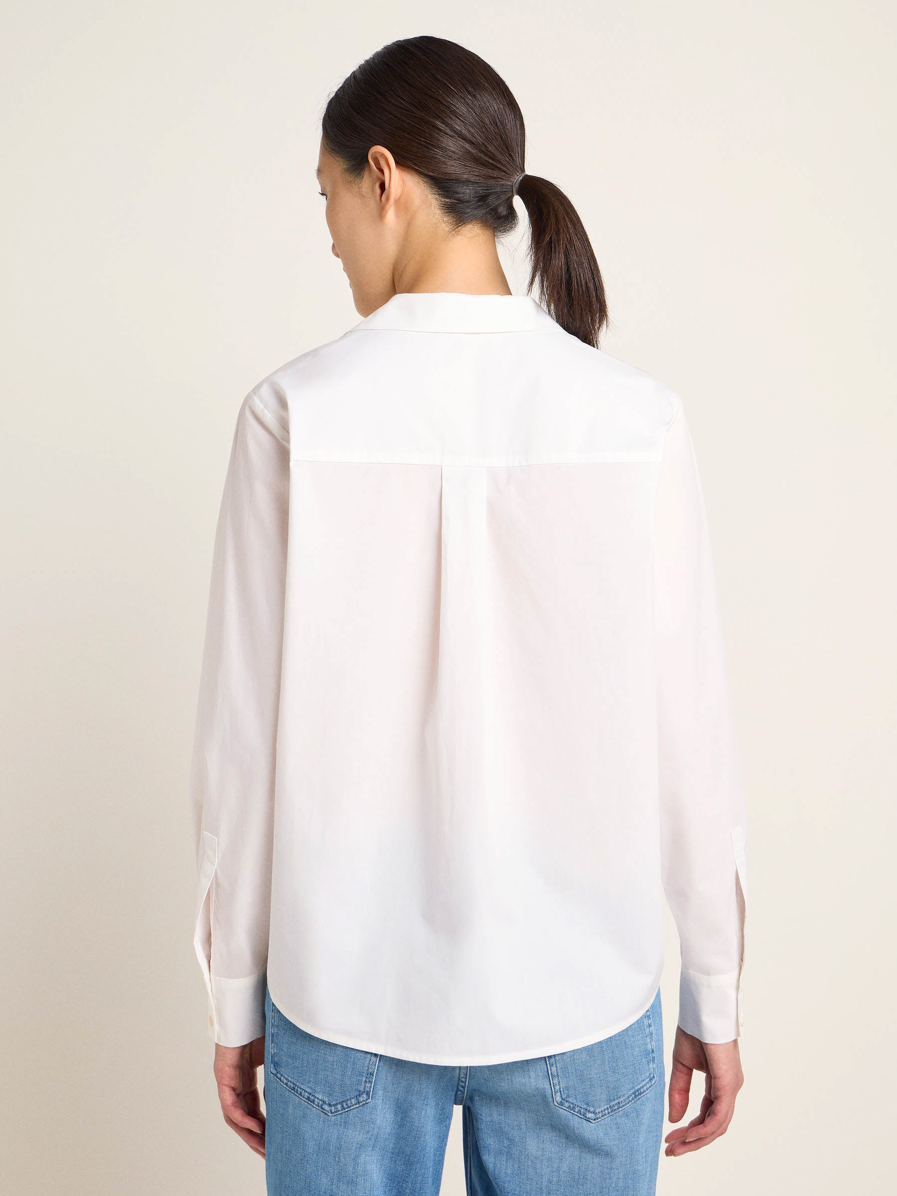 Frau trägt weiße Bluse und Jeans von hinten