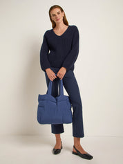 Frau mit Pullover, Hose und großer Tasche posiert.