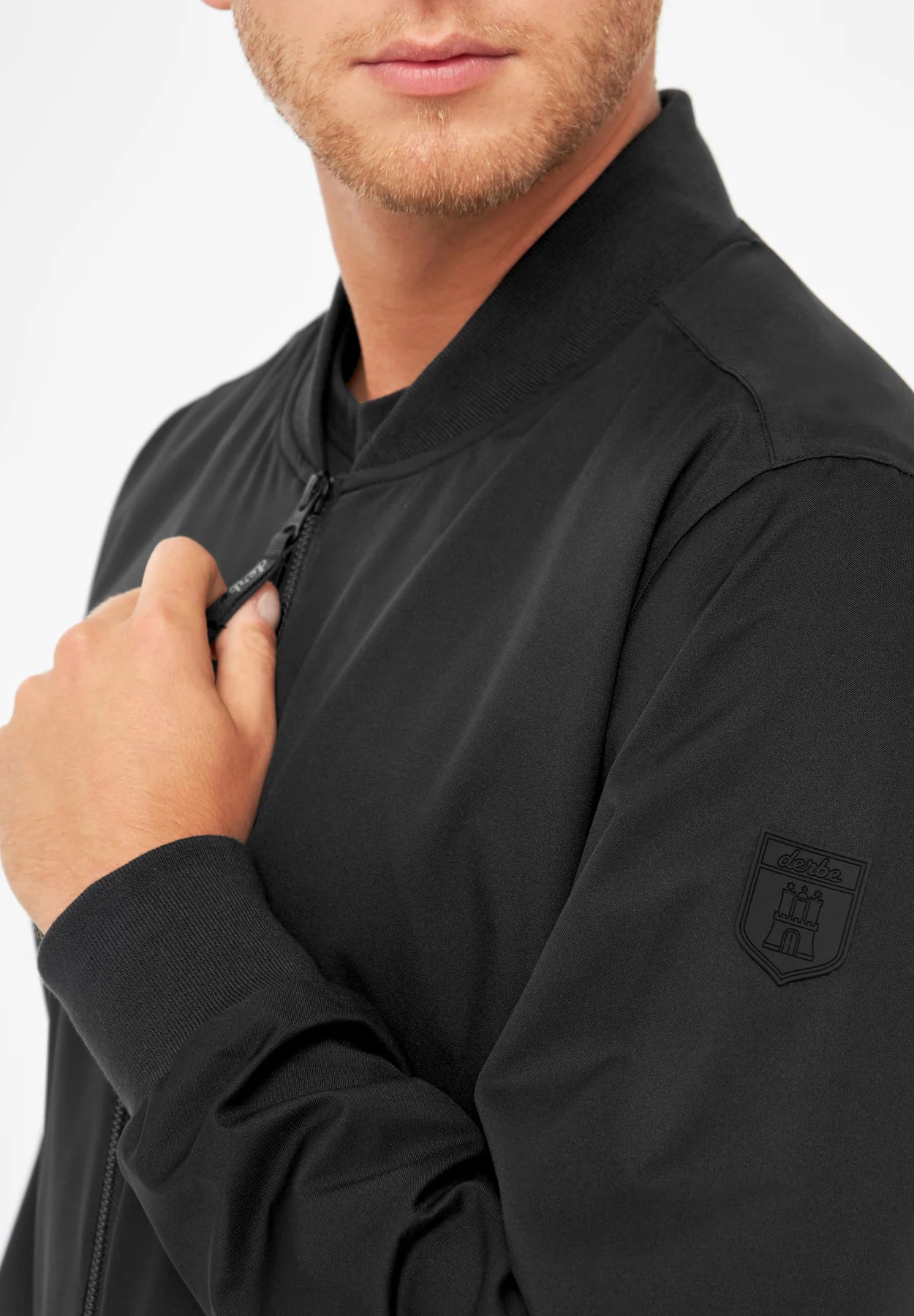 Mann zieht schwarze Jacke mit Logo zu.
