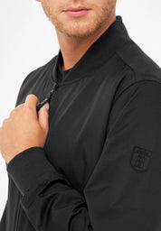 Mann zieht schwarze Jacke mit Logo zu.