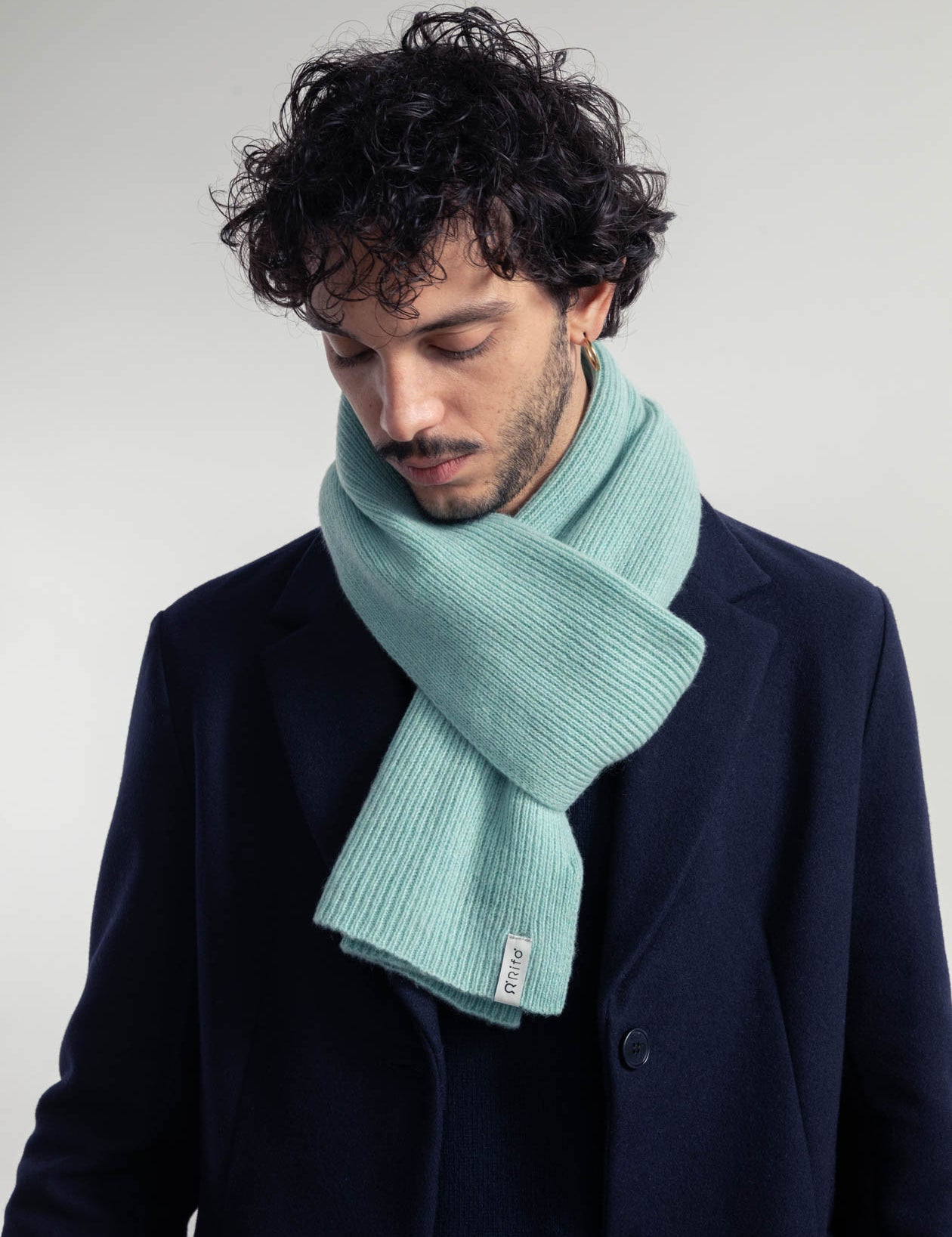 Mann mit Locken trägt Schal und dunklen Mantel