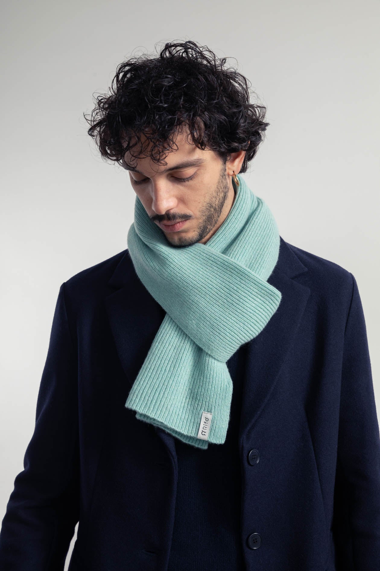 Mann mit Locken trägt Schal und dunklen Mantel