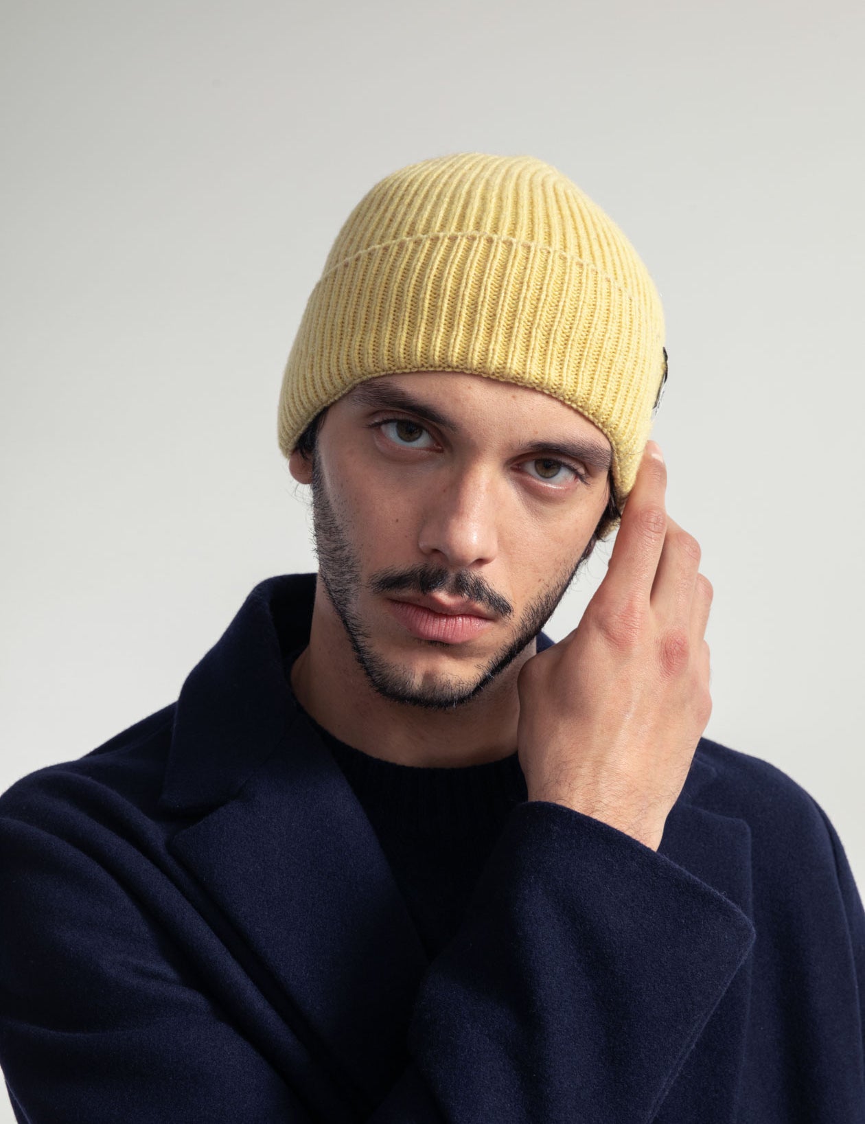 Mann in gelber Mütze und blauem Mantel berührt Gesicht