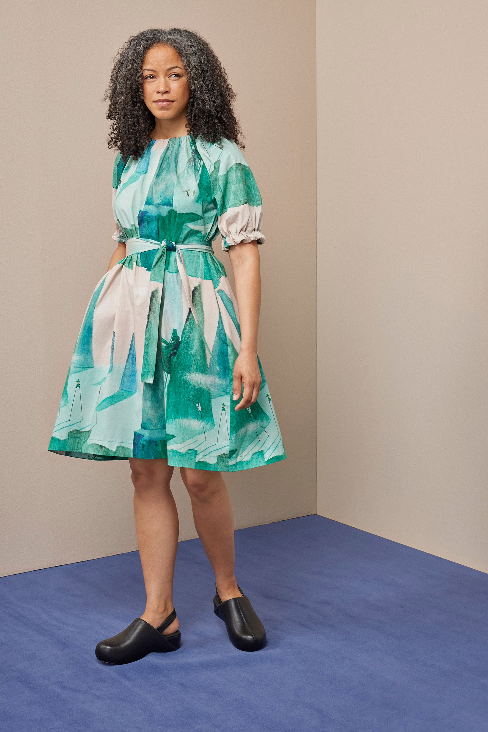 Frau in gemustertem Kleid steht auf blauem Teppich.