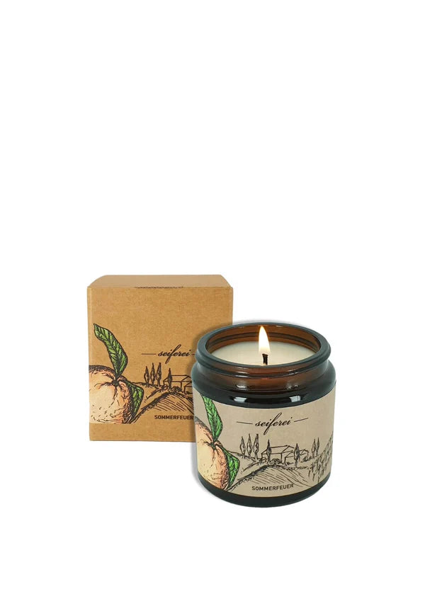 Duftkerze im Glas mit Verpackung und brennender Flamme.