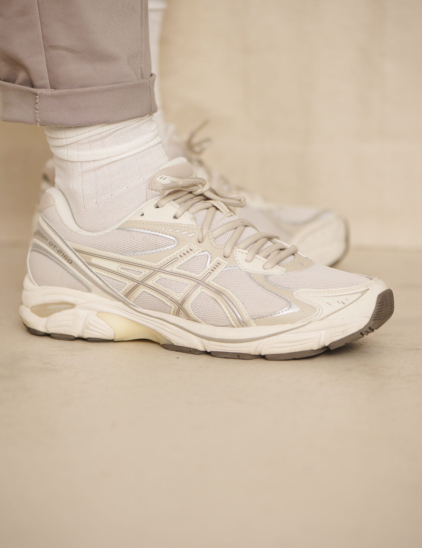 Person trägt weiße Sneaker und beige Hose
