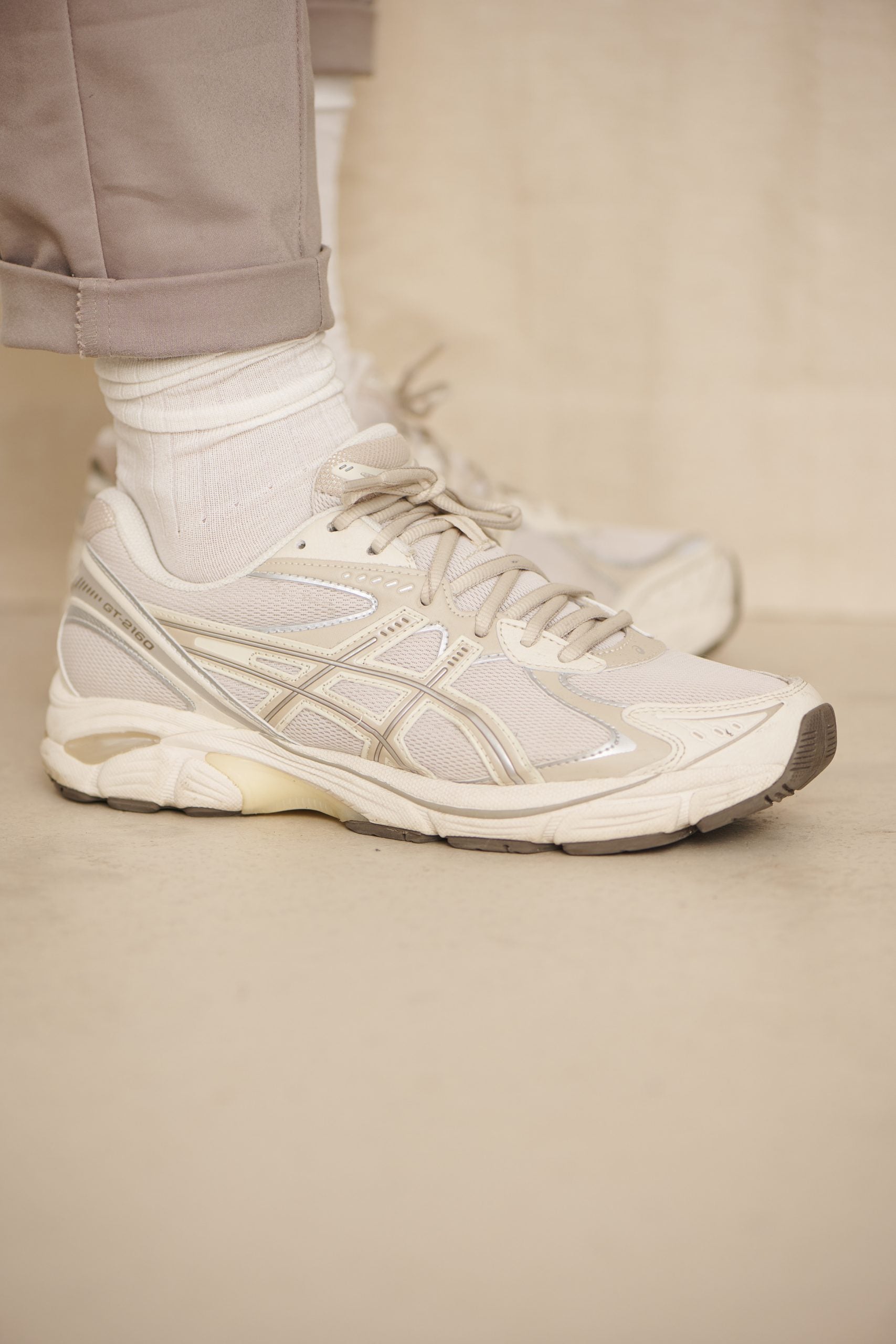 Person trägt weiße Sneaker und beige Hose
