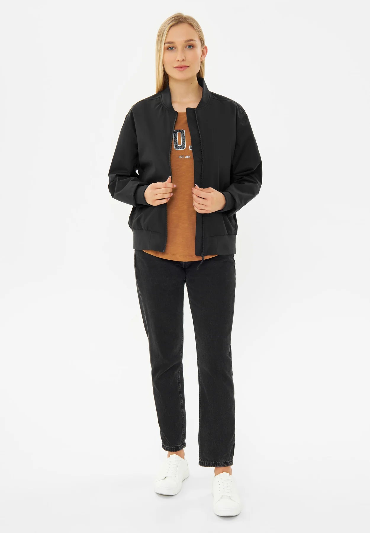 Frau in Bomberjacke und schwarzen Jeans steht.