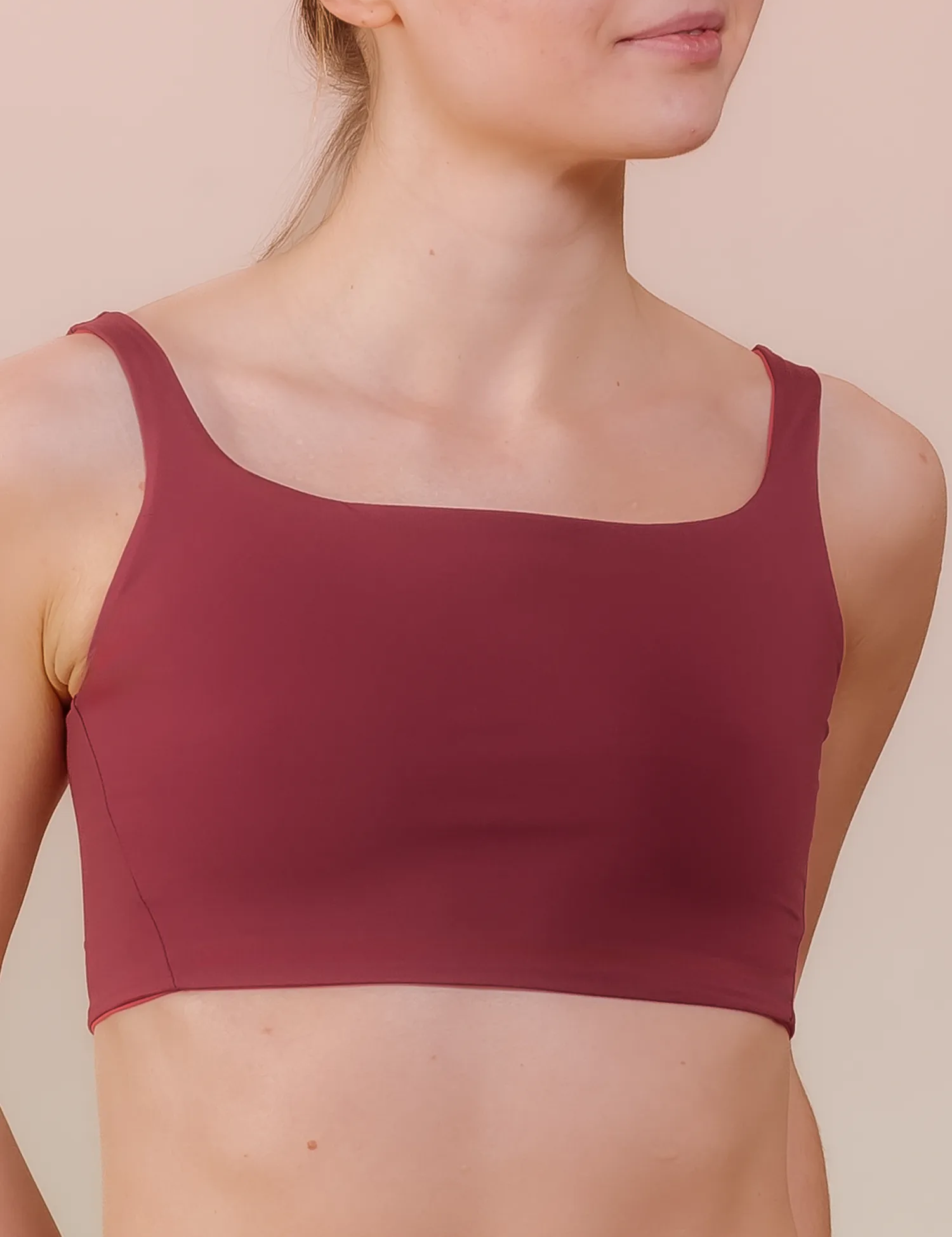 Frau in bordeauxrotem Sport-Top, neutraler Hintergrund.