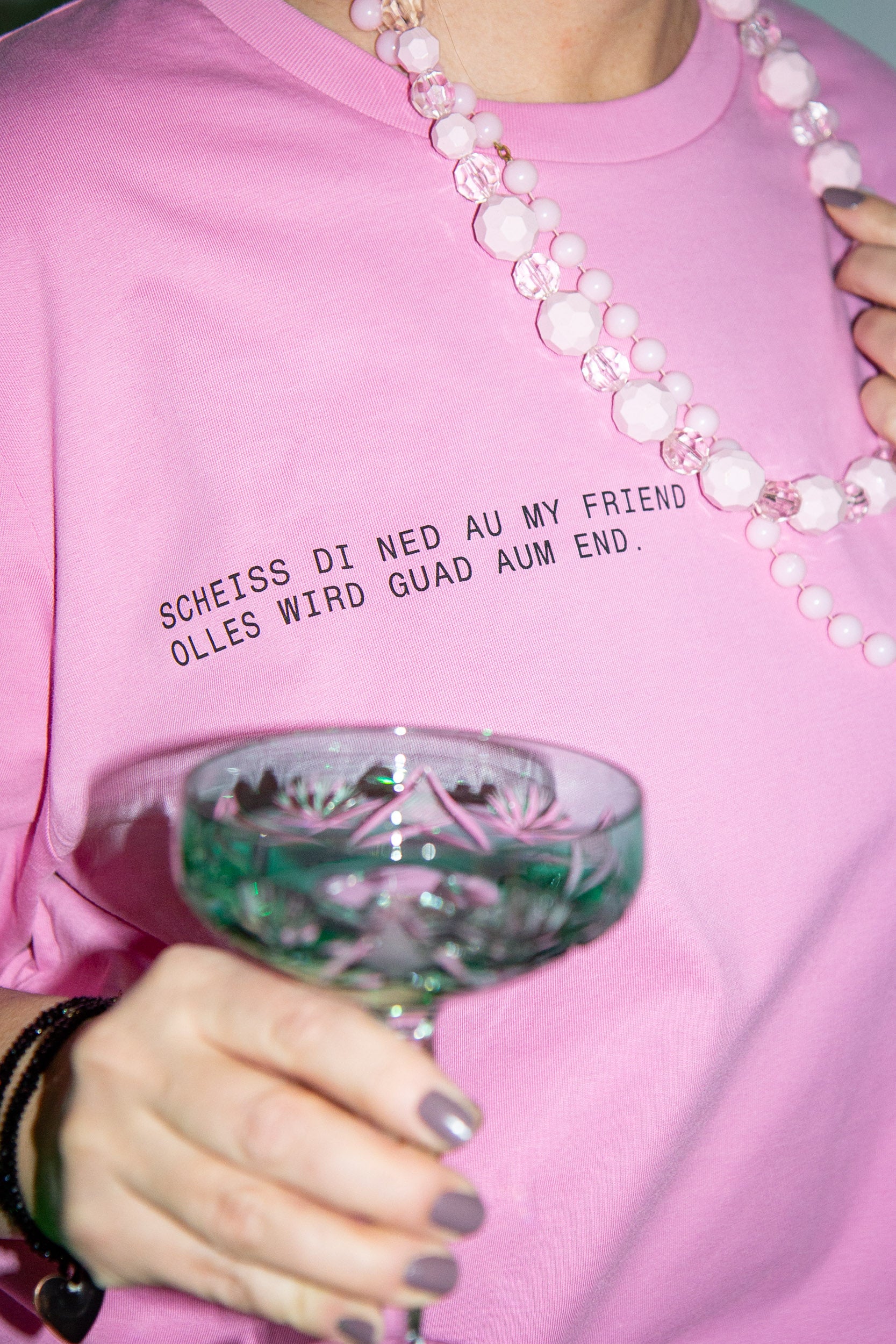 Person hält Glas mit rosa Pullover und Perlenkette