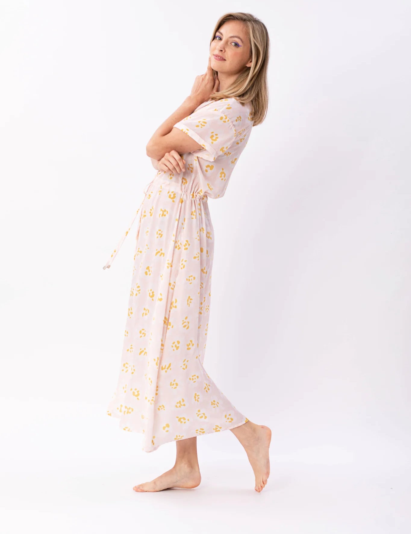 Frau in pastellfarbenem, geblümtem Maxikleid posiert lächelnd.