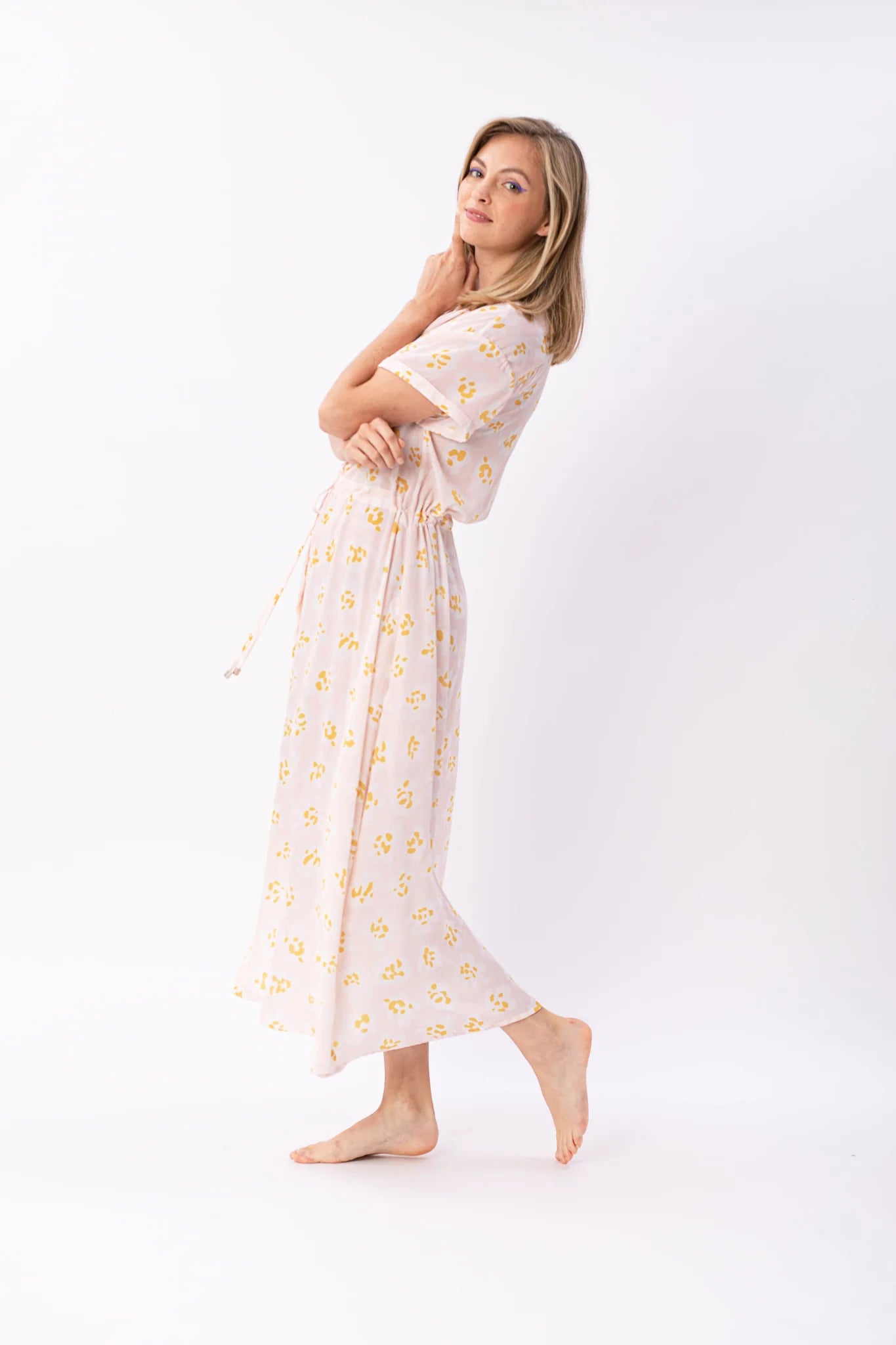 Frau in pastellfarbenem, geblümtem Maxikleid posiert lächelnd.