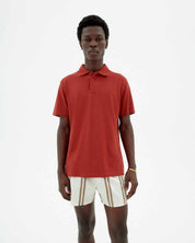 Junger Mann trägt rotes Poloshirt und weiße Shorts