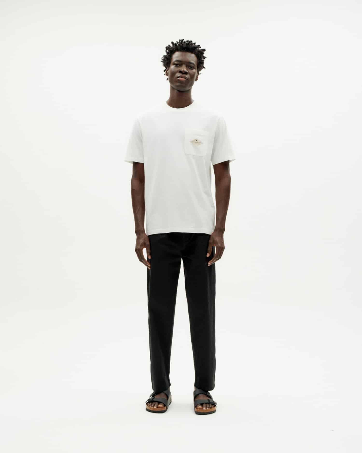 Mann in weißem T-Shirt und schwarzen Hosen steht.