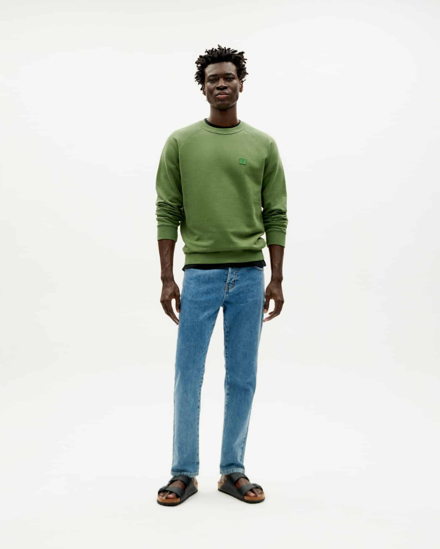 Mann in grünem Pullover und Jeans steht.