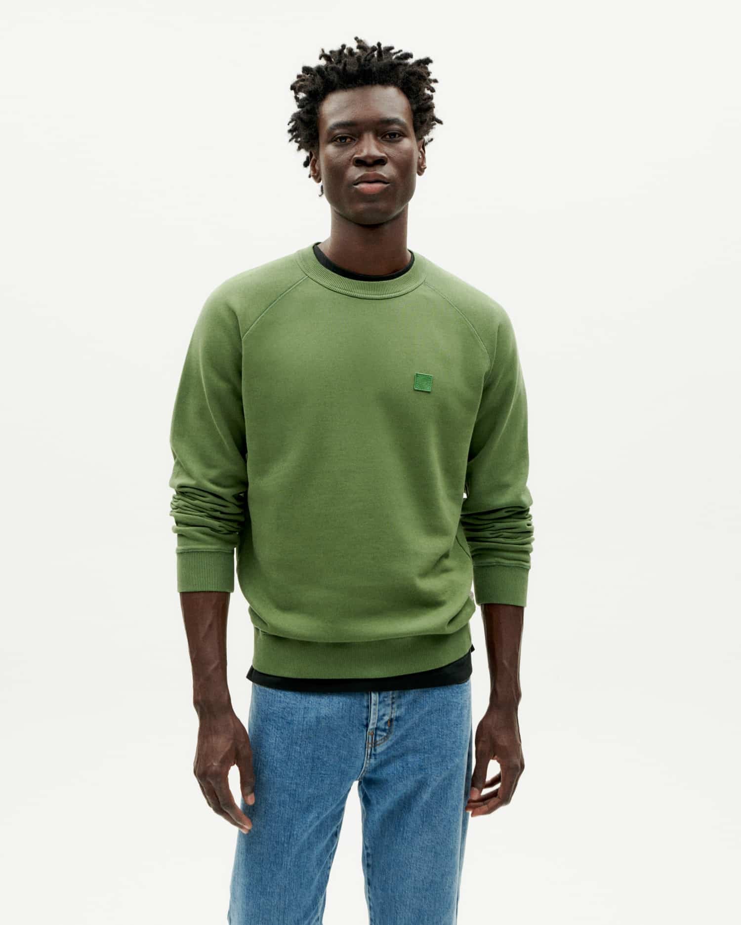 Mann in grünem Sweatshirt und Jeans steht.