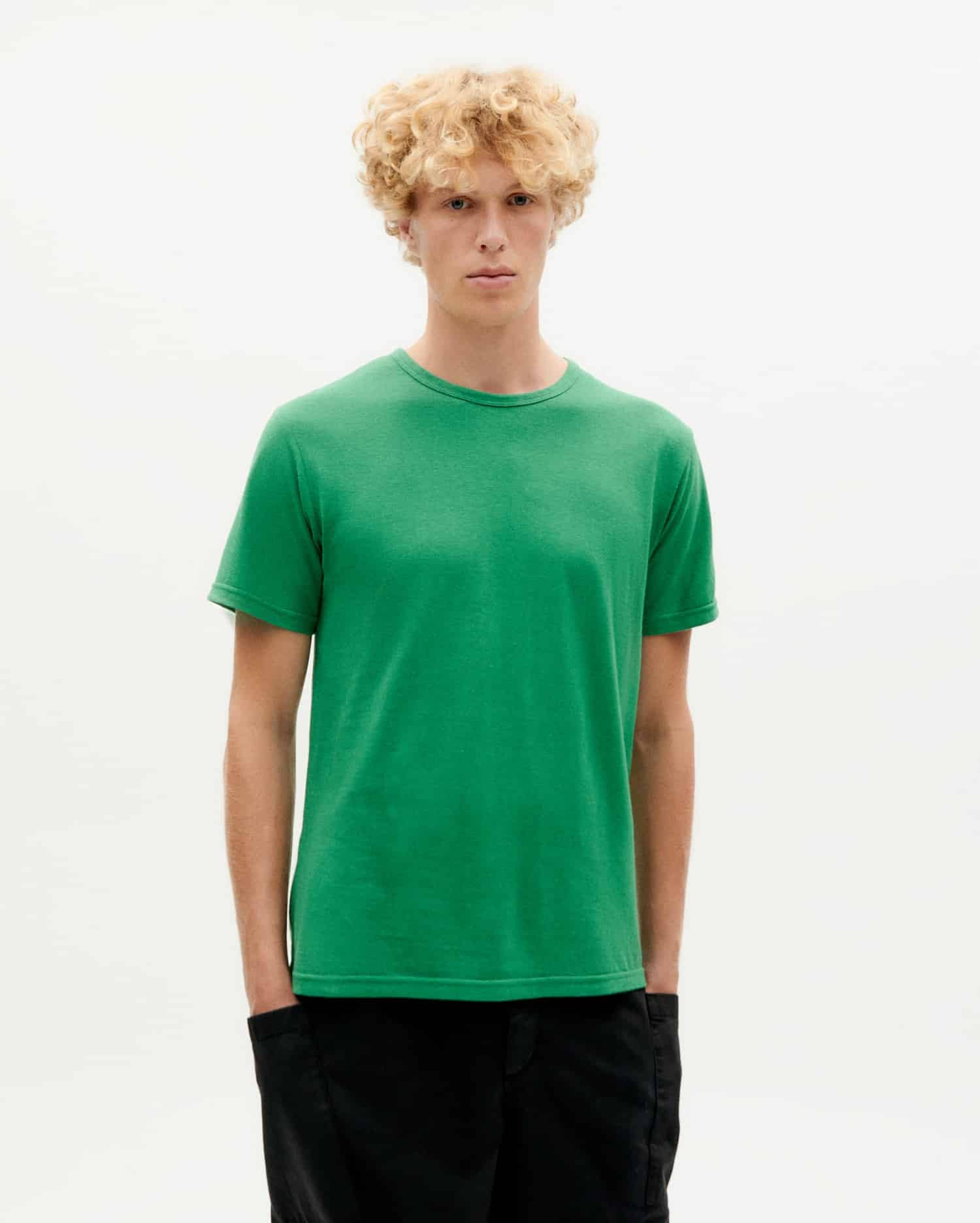 Junger Mann in grünem T-Shirt steht vor weißem Hintergrund.
