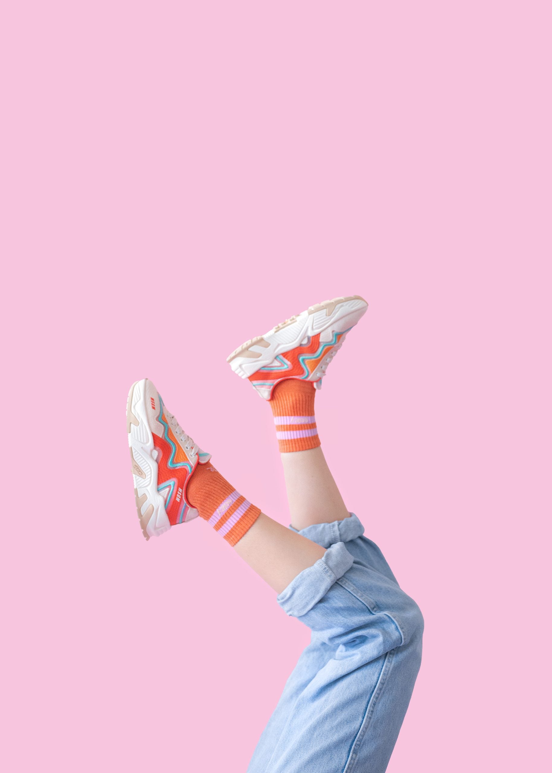 Beine in Jeans und bunten Sneakers, rosa Hintergrund