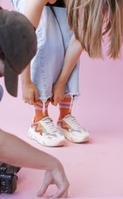Frau zieht Sneakers vor rosa Hintergrund an