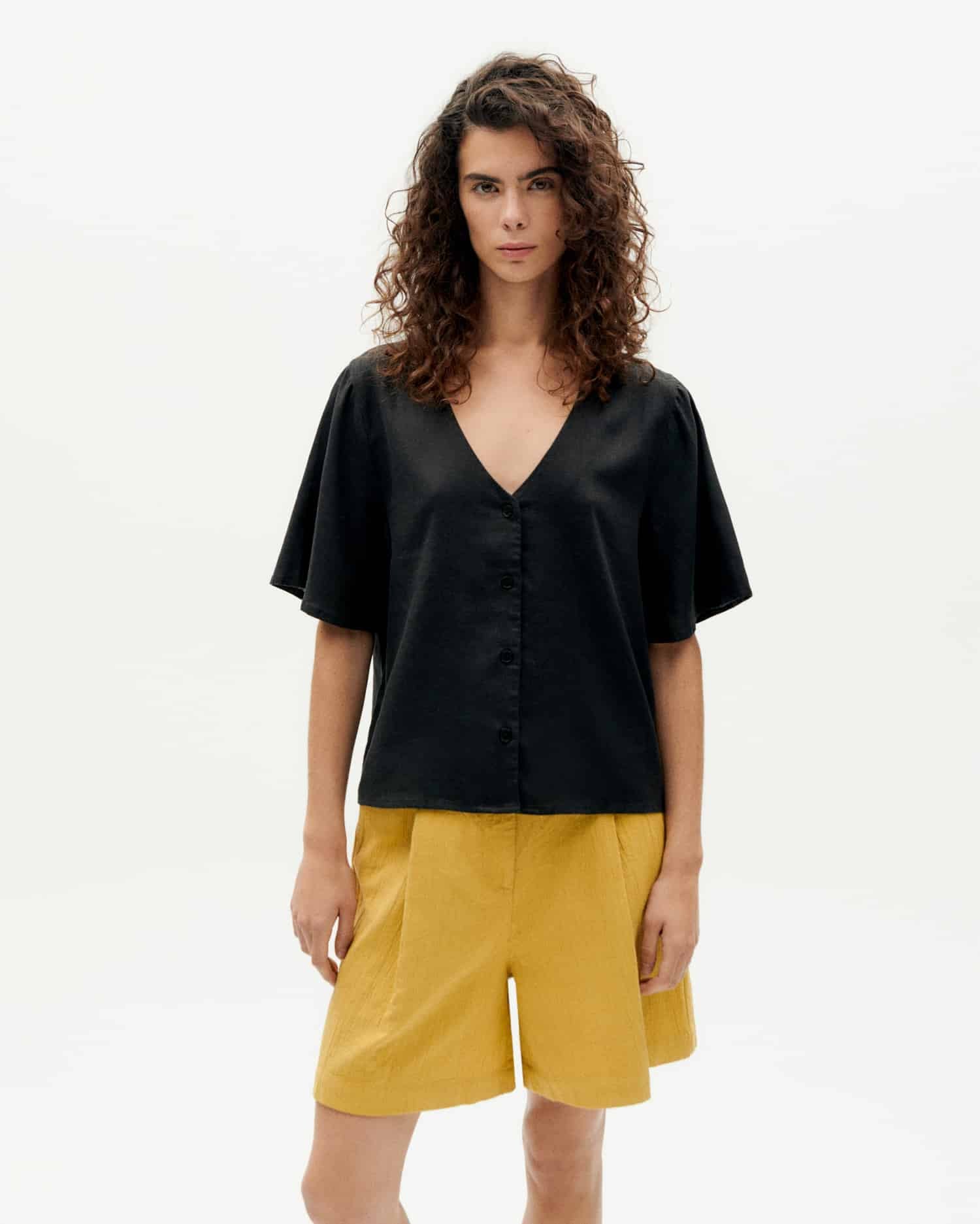 Frau in schwarzem Top und gelben Shorts steht.