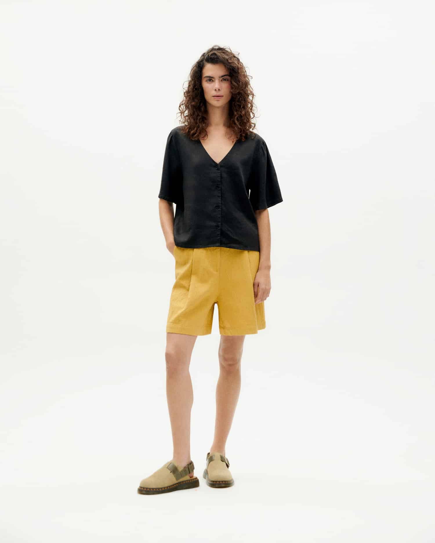 Model in schwarzer Bluse und gelber Shorts.
