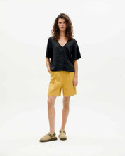 Model in schwarzer Bluse und gelber Shorts.