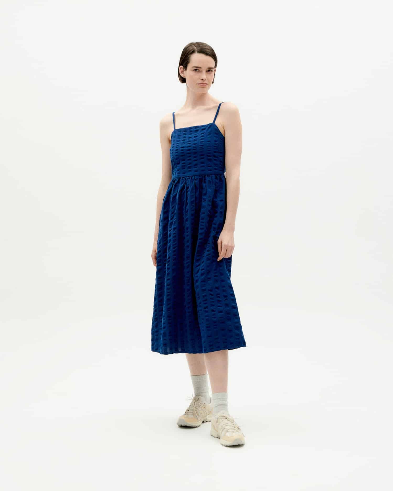 Frau in blauem Midikleid und weißen Sneakers.