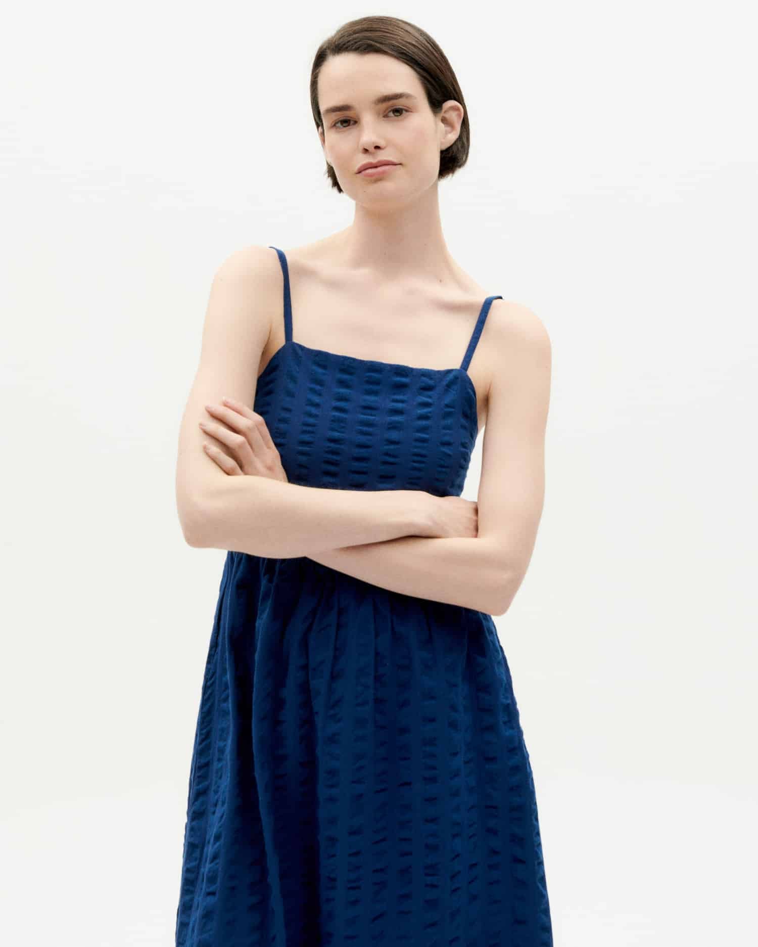 Frau in blauem Kleid steht mit verschränkten Armen.